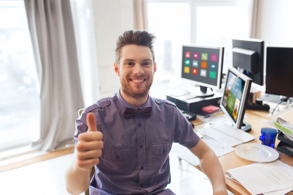 7 Essential Web Solutions To Boost Your Company'S Productivity 1 man giving thumb up with a big smile on his face and computer screens in the background