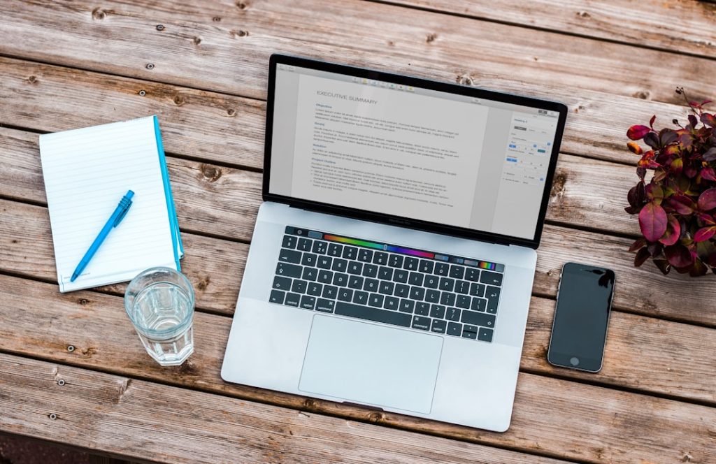 mackbook pro with a cup of water, notebook and an iphone